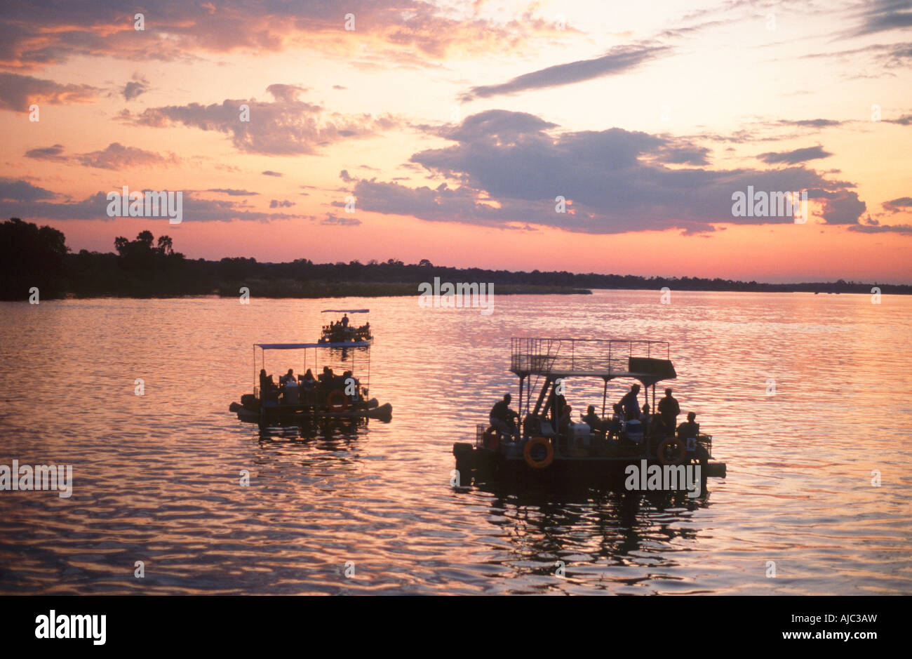 Coucher de soleil sur le fleuve Zambèze avec trois radeaux Croisière en premier plan Banque D'Images