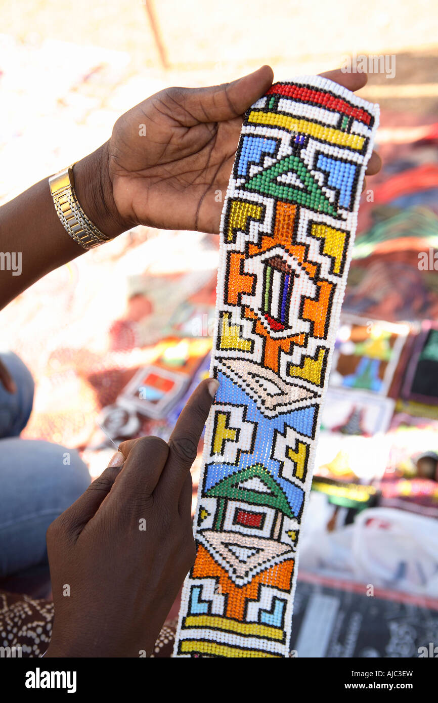 Femme tenant une ceinture perlée en pointant sur l'image aux couleurs vives des motifs africains dans son artisanat Banque D'Images
