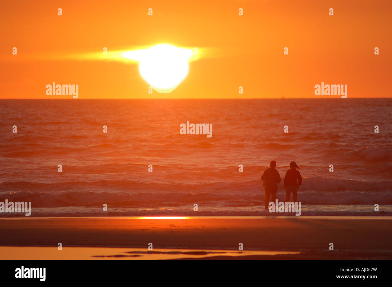 Deux personnes regardant le coucher du soleil sur la plage de Fistral, Newquay, Cornwall, UK Banque D'Images