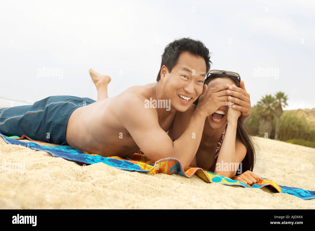 Jeune couple couché sur la plage, riant, se cachant les yeux de l'homme femme Banque D'Images