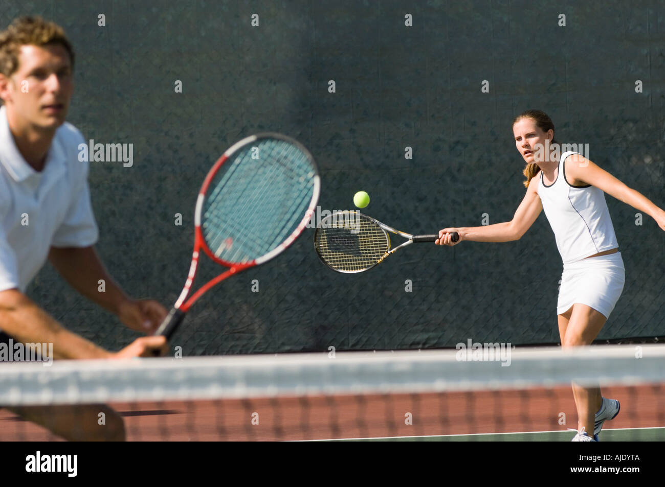 Double mixte player hitting tennis ball, partenaire debout près de net Banque D'Images