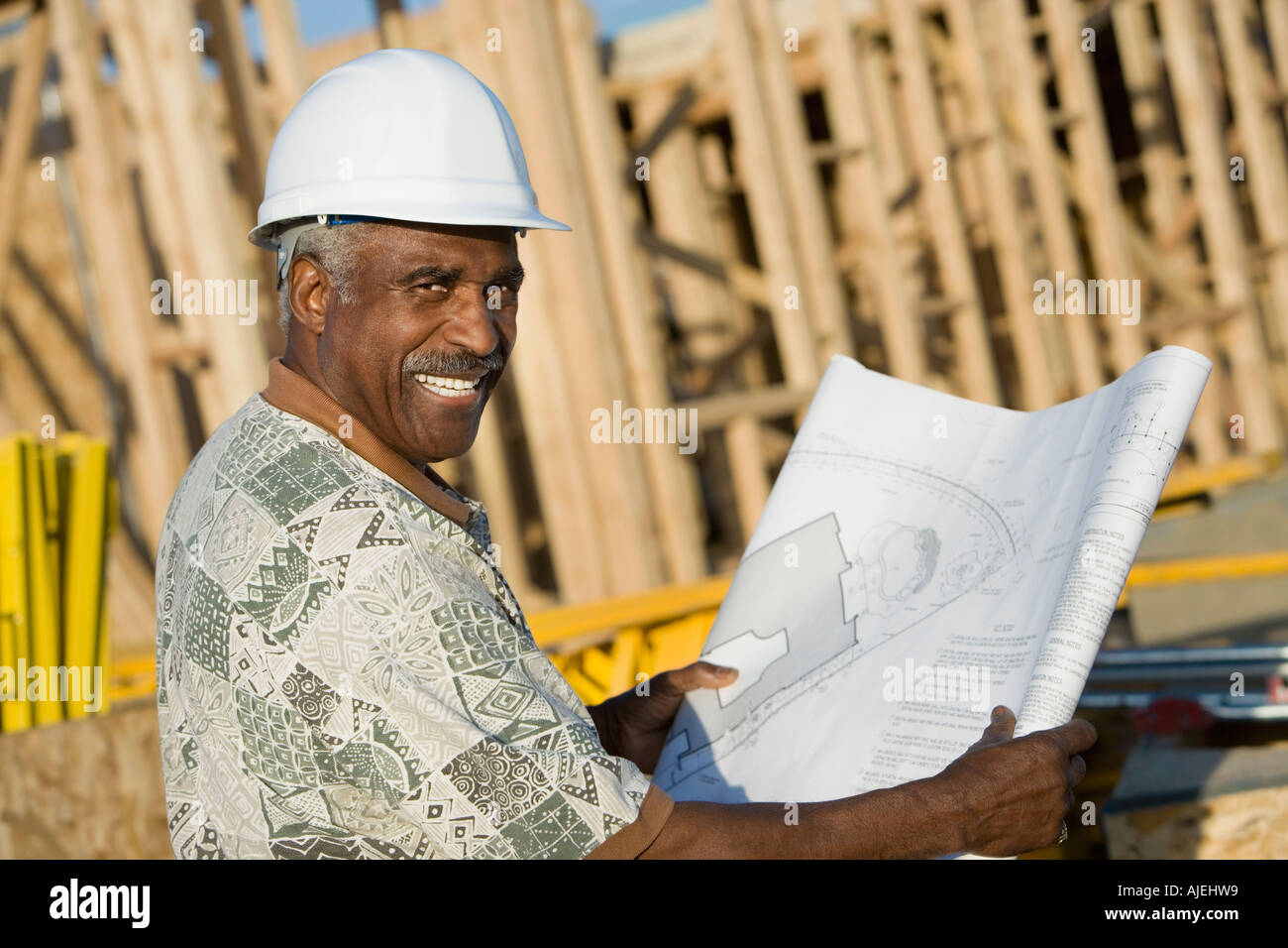Homme d'âge moyen dans la région de hard hat holding blueprint in front of house construction site Banque D'Images