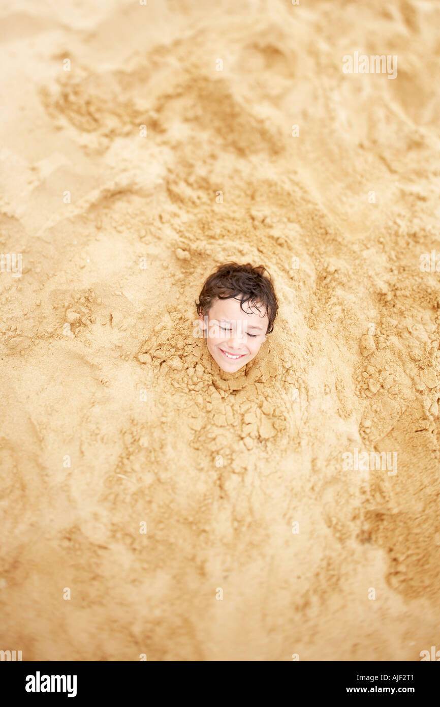 Garçon enterré dans le sable jusqu'à son cou, vue de dessus Banque D'Images