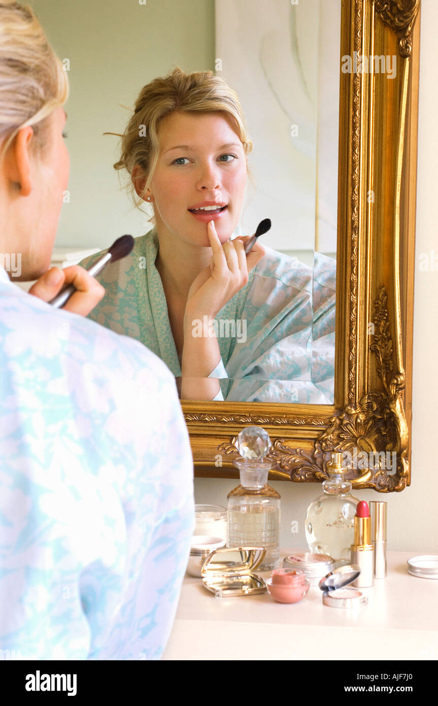 Femme en peignoir assis, l'application du maquillage, à la recherche dans le miroir Banque D'Images