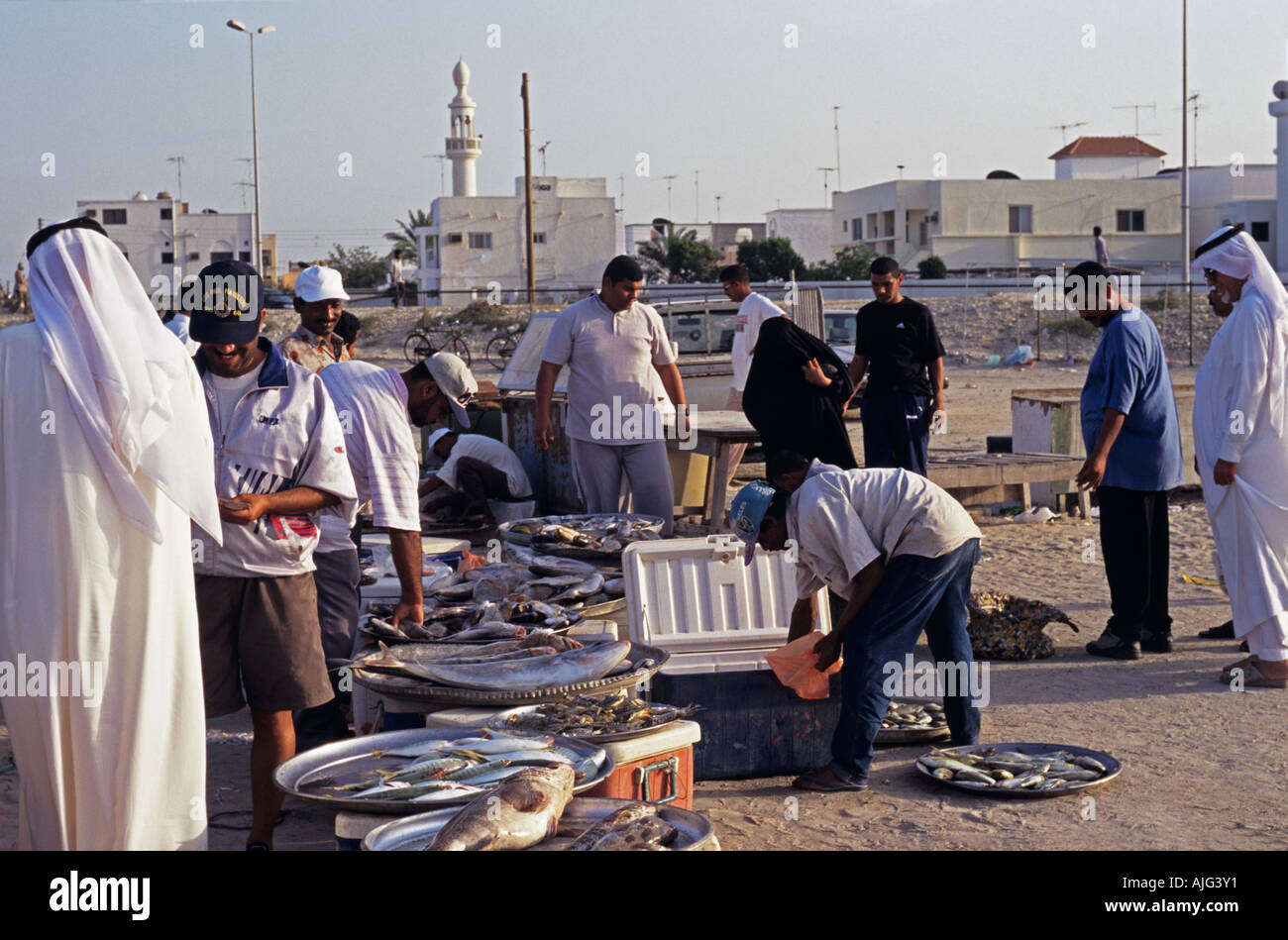 Les hommes en costume traditionnel arabe plus femme en burqa d'acheter du poisson au marché, Bahreïn Banque D'Images