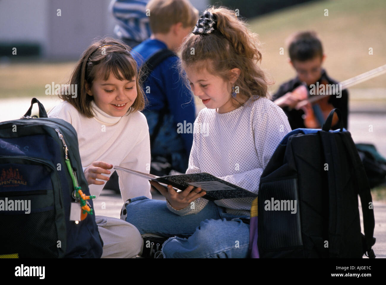 Les élèves de sexe féminin de race blanche à faire leurs devoirs avec leurs ordinateurs portables tout en restant assis dans l'herbe avec leurs sacs à dos Banque D'Images