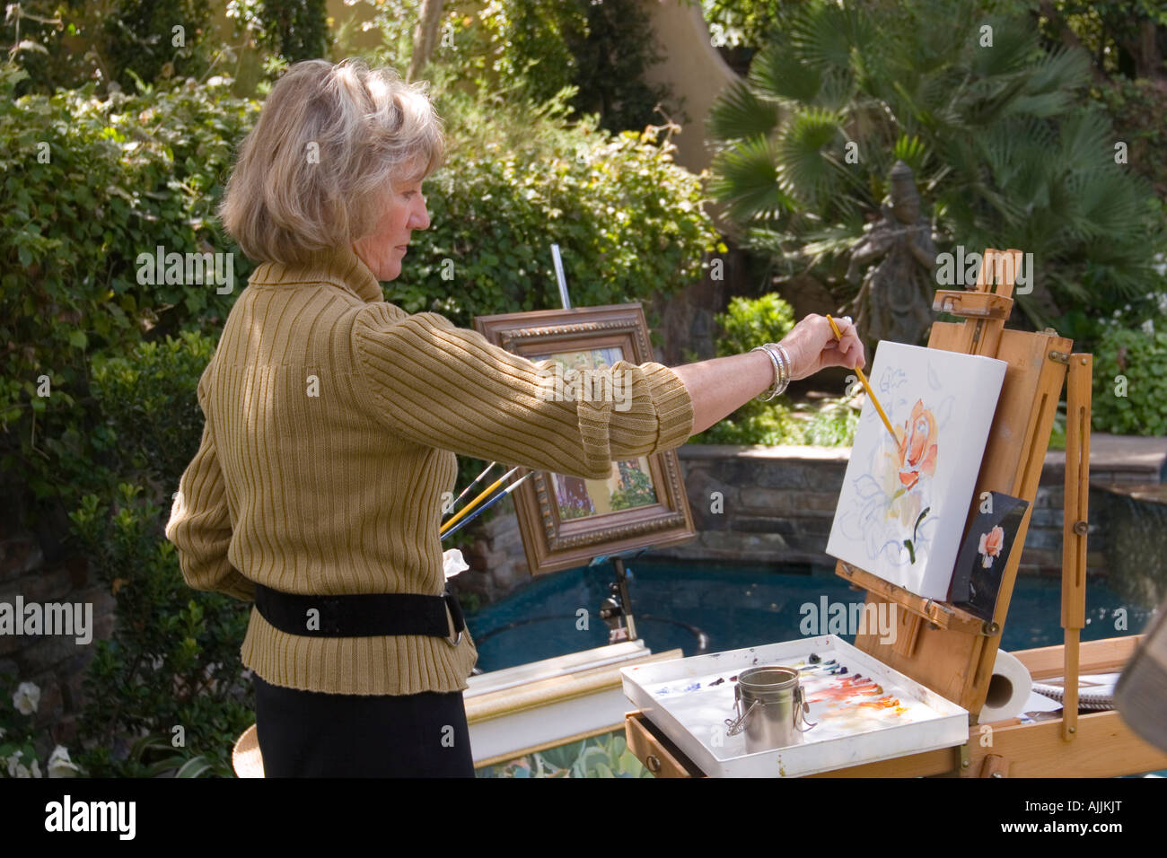 Une femme debout devant un chevalet, bénéficie d'la peinture de plein air dans un jardin de banlieue. Banque D'Images