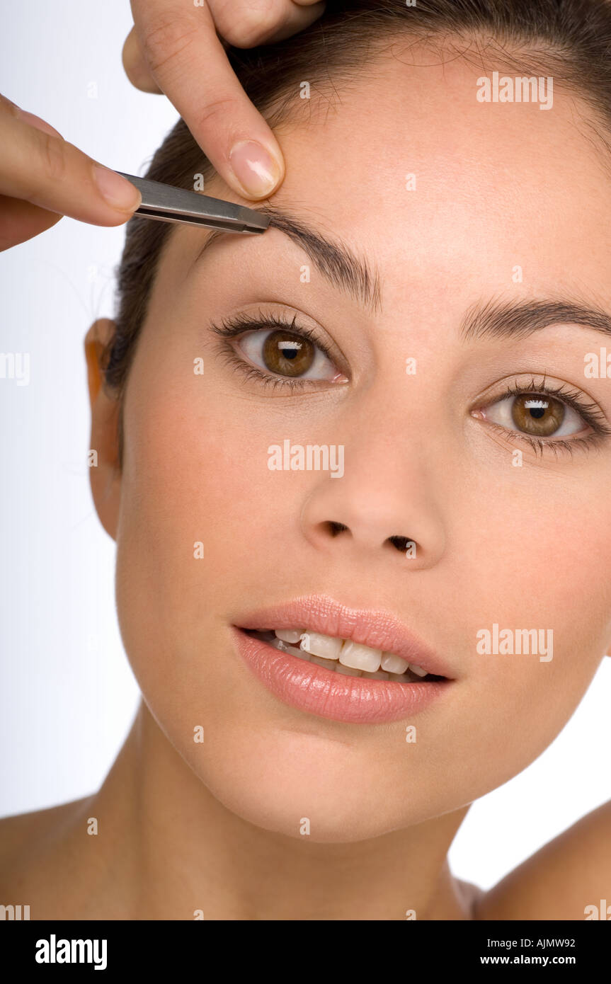 Une jeune femme plucking her eyebrows Banque D'Images