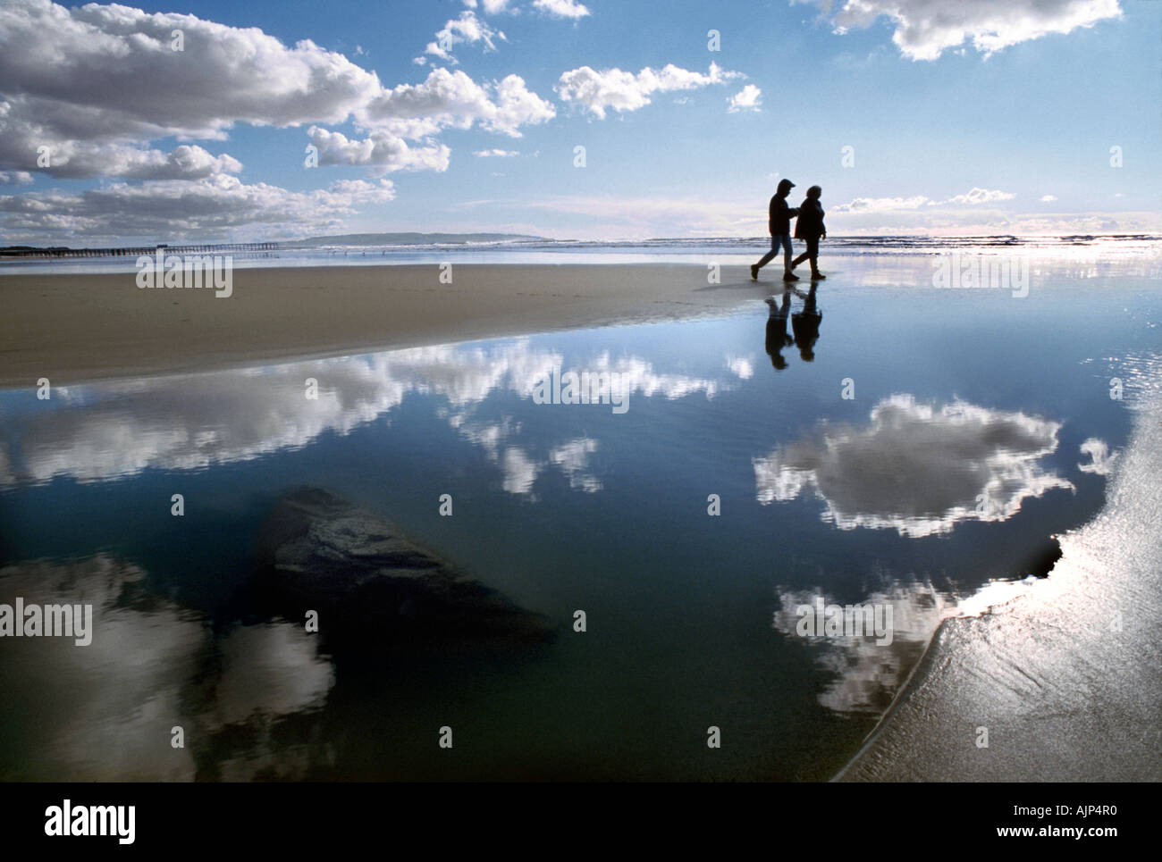 Un couple marche le long d'une plage de Californie alors que les flaques, les nuages et la réflexion autour de l'homme et de la femme. Banque D'Images