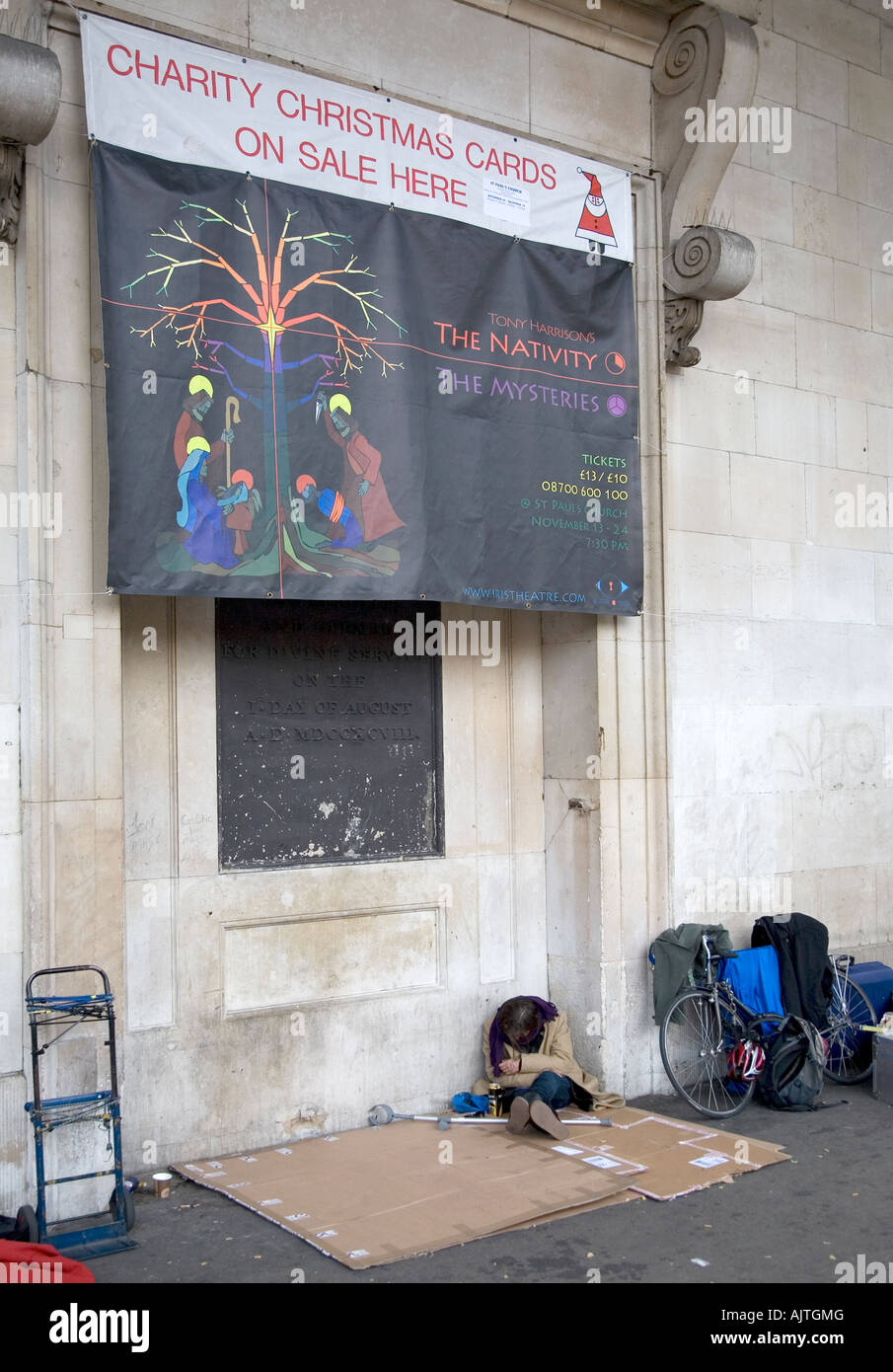 Une personne sans-abri dormir sur du carton. Au-dessus pend un signe de l'église au sujet des cartes de Noël Banque D'Images