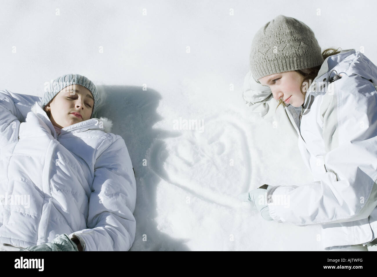 Teenage Girls lying on Snow, un coeur avec les initiales de dessin dans la neige Banque D'Images