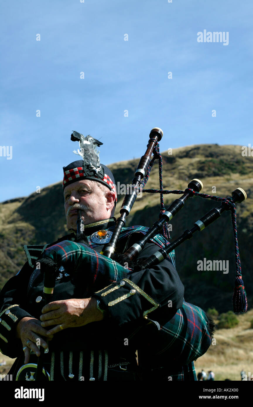 Piper solitaire jouer cornemuse dans le parc Holyrood Edinburgh Scotland avec Arthur siège dans l'arrière-plan Banque D'Images