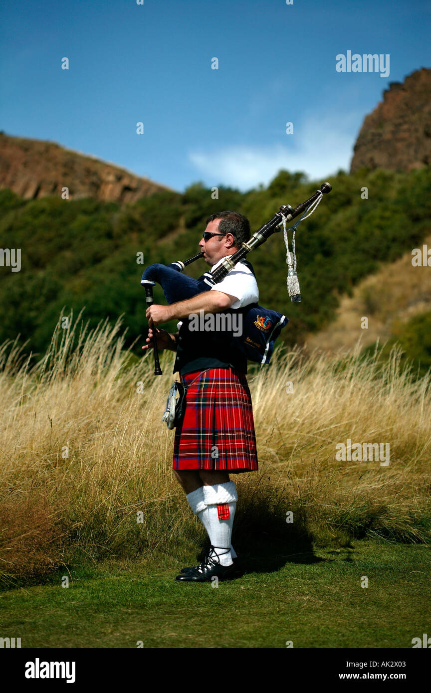 Piper solitaire jouer cornemuse dans le parc Holyrood Edinburgh Scotland avec Salisbury Crags dans l'arrière-plan Banque D'Images