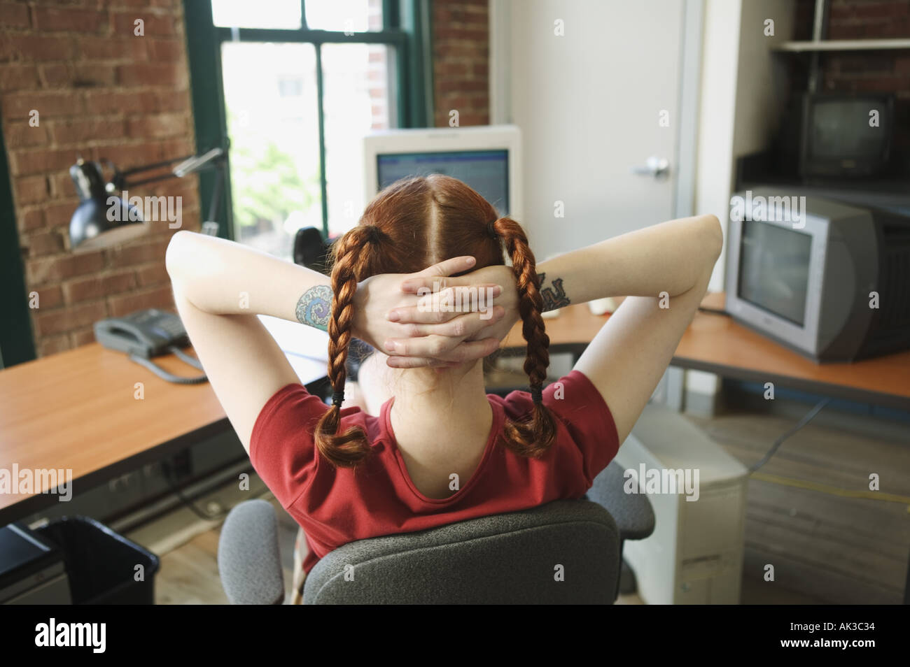 Femme aux cheveux rouges s'adossant à son bureau 24 Banque D'Images Femme aux cheveux rouges s'adossant à son bureau 24 Banque D'Images