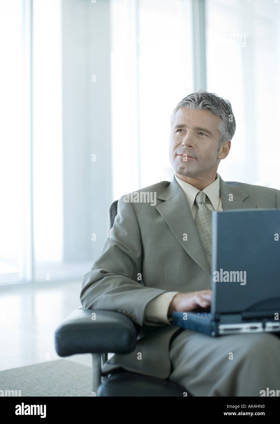 Businessman using laptop in office lobby Banque D'Images