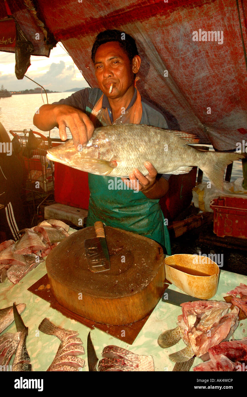 Poissonnier fumeurs et tenant un poisson dans un marché à Kota Kinabalu à Bornéo Banque D'Images