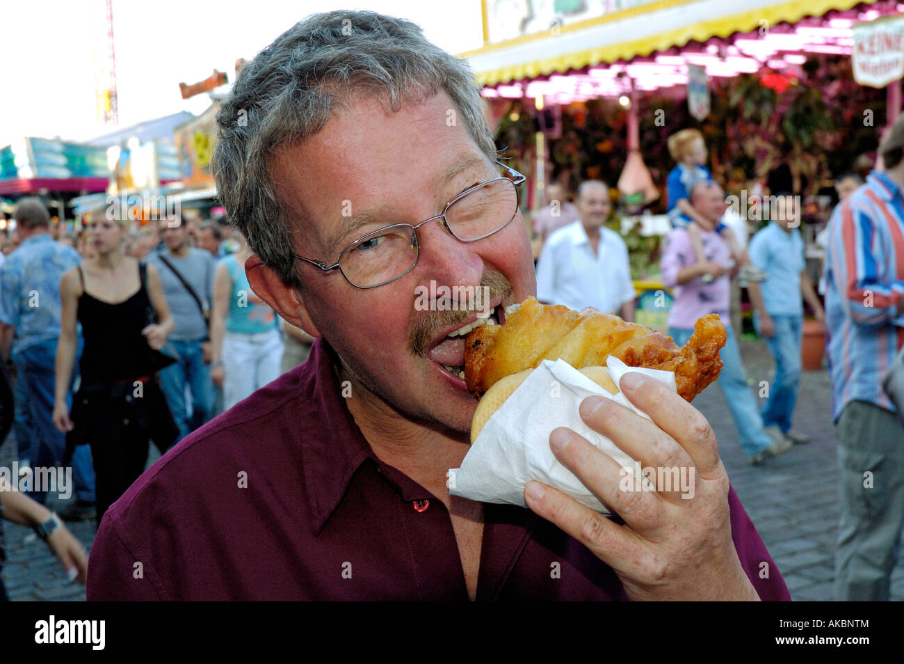 Homme d'âge moyen avec des lunettes mordre dans un Fischbrötchen (rouleau de poissons) à Düsseldorf Kirmes (fête foraine), Allemagne 2007 Banque D'Images