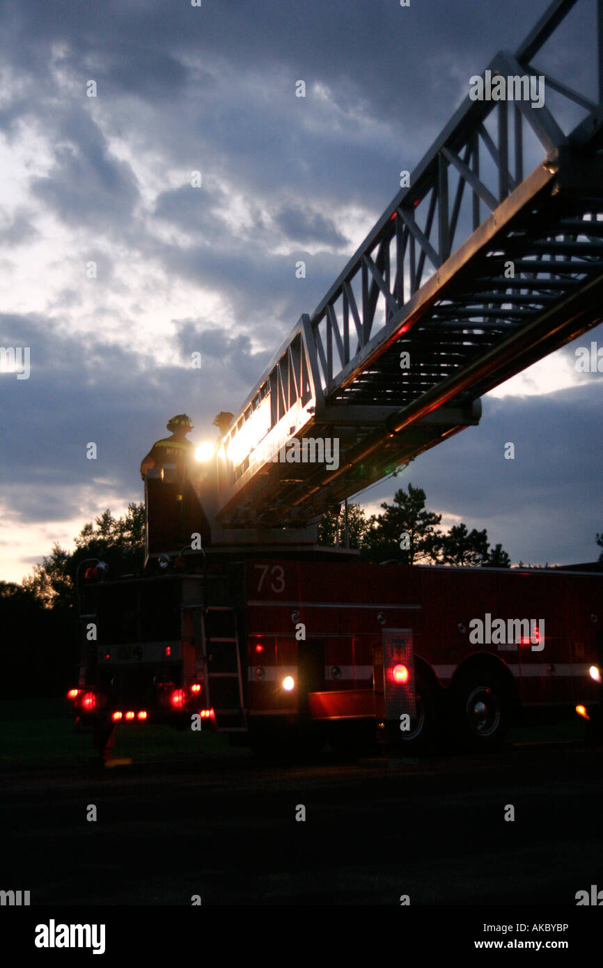 Deux pompiers aux commandes de l'échelle d'un camion d'incendie au coucher du soleil Banque D'Images