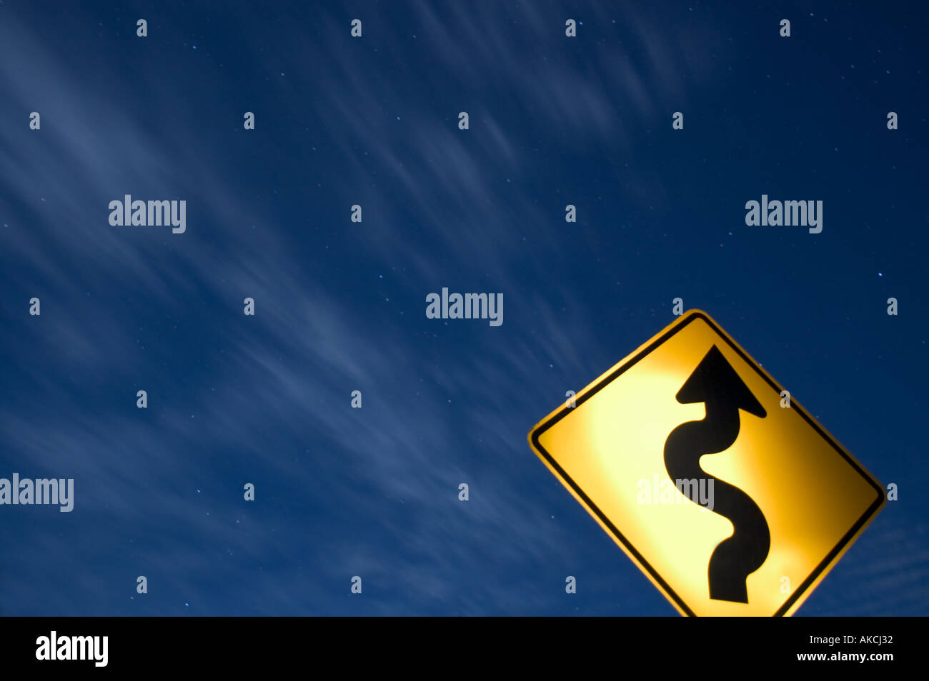 Curvy road sign against blue sky de nuit pendant une longue exposition avec le déplacement des nuages. © Craig M. Eisenberg Banque D'Images