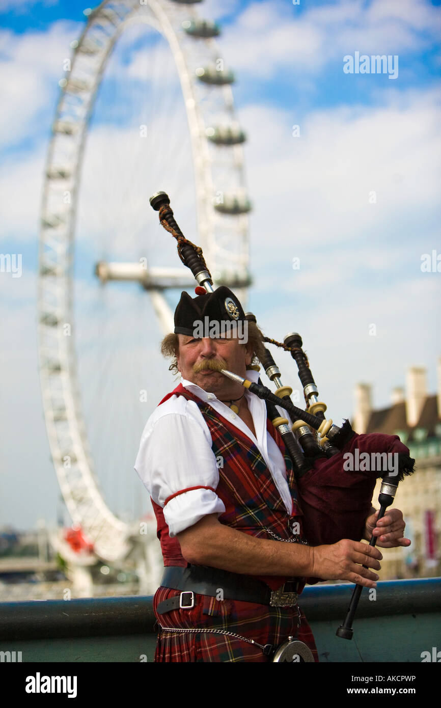Un Écossais en kilt, de la rue Piper jouant sa cornemuse sur Hungerford Bridge avec le London Eye en arrière-plan. Banque D'Images