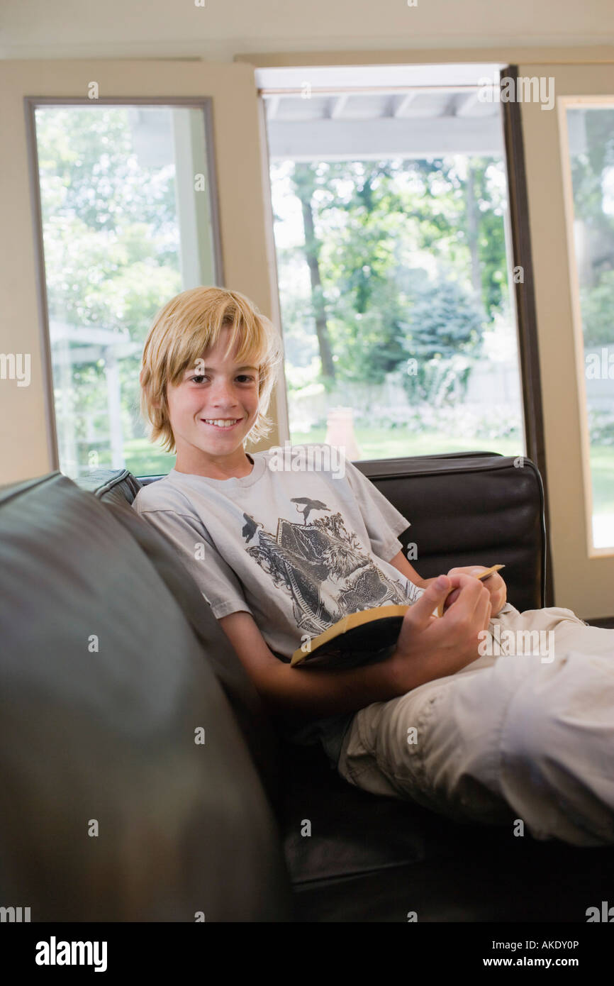 Portrait off boy (10-12) sitting on sofa with book, smiling Banque D'Images