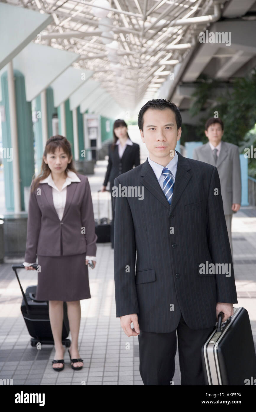 Businessman walking et tenant sa valise à trois cadres d'affaires dans l'arrière-plan Banque D'Images