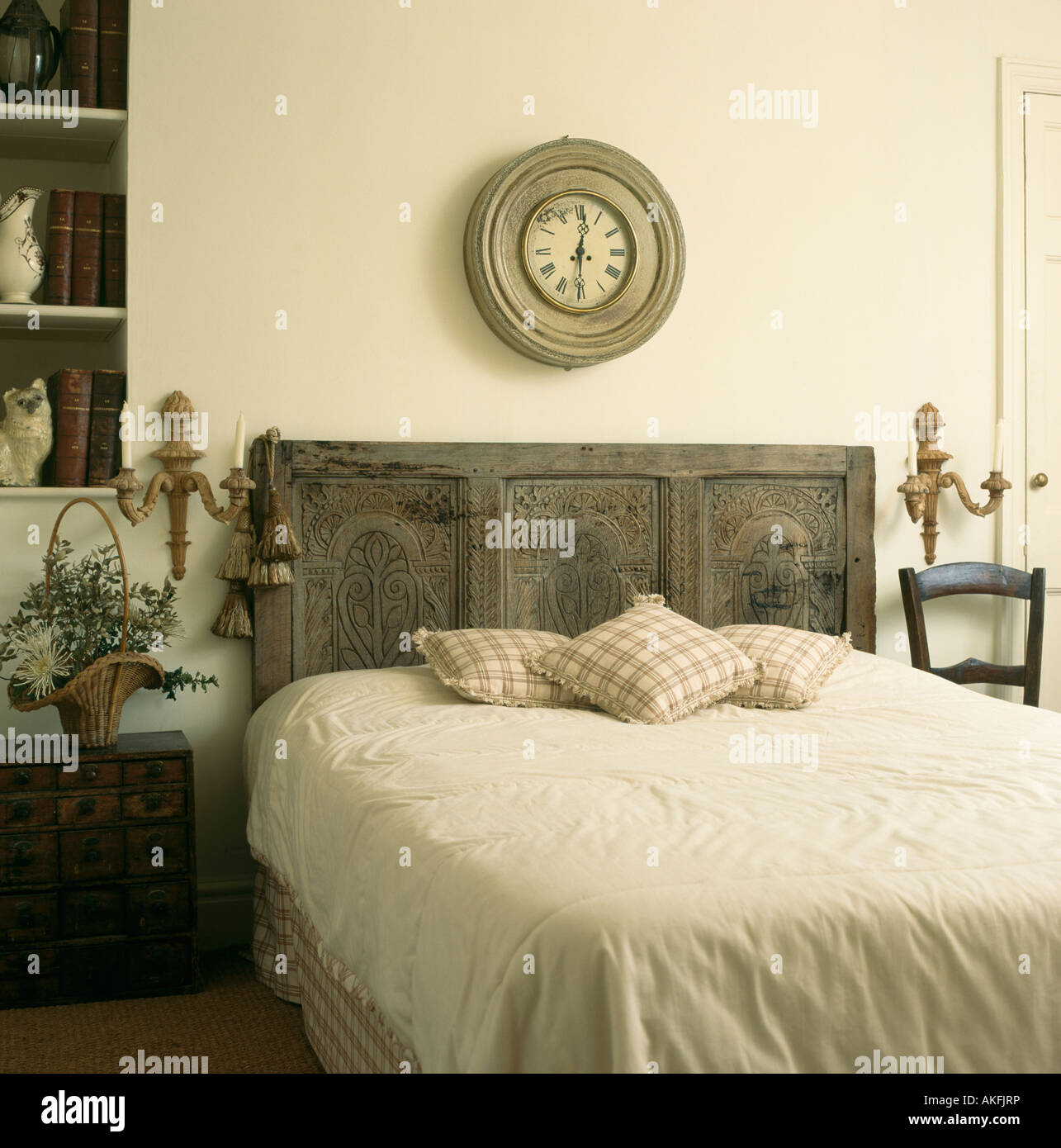 Réveil en bois en détresse circulaire au-dessus de lit avec tête de lit  ancien sculpté récupérée dans une chambre avec draps crème Photo Stock -  Alamy