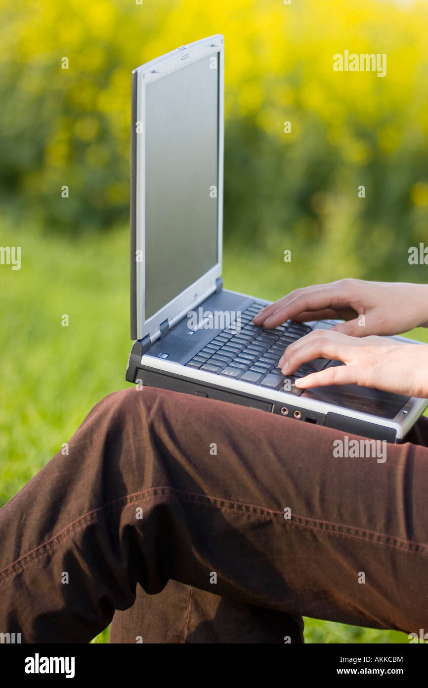 Femme travaillant avec un ordinateur portable sur ses genoux à l'extérieur dans un pré Banque D'Images