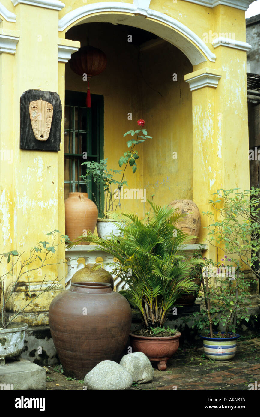 Colonnade voûtée jaune, pots et plantes dans une cour pavée de briques de la maison, Nguyen Thi Minh Khai St, Hoi An, Viet Nam Banque D'Images