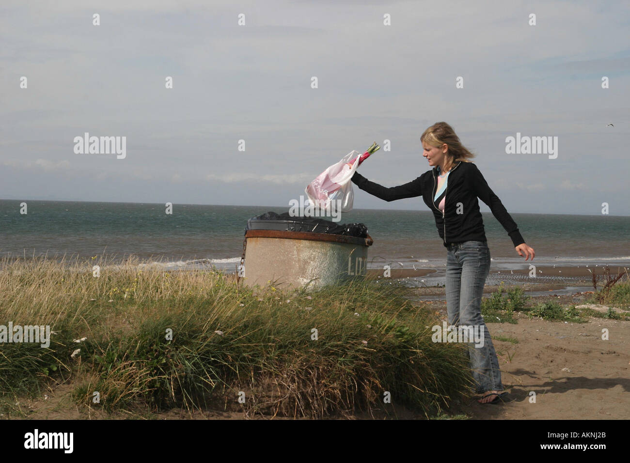Girl putting ordures dans une poubelle près de la mer en Cumbria Banque D'Images