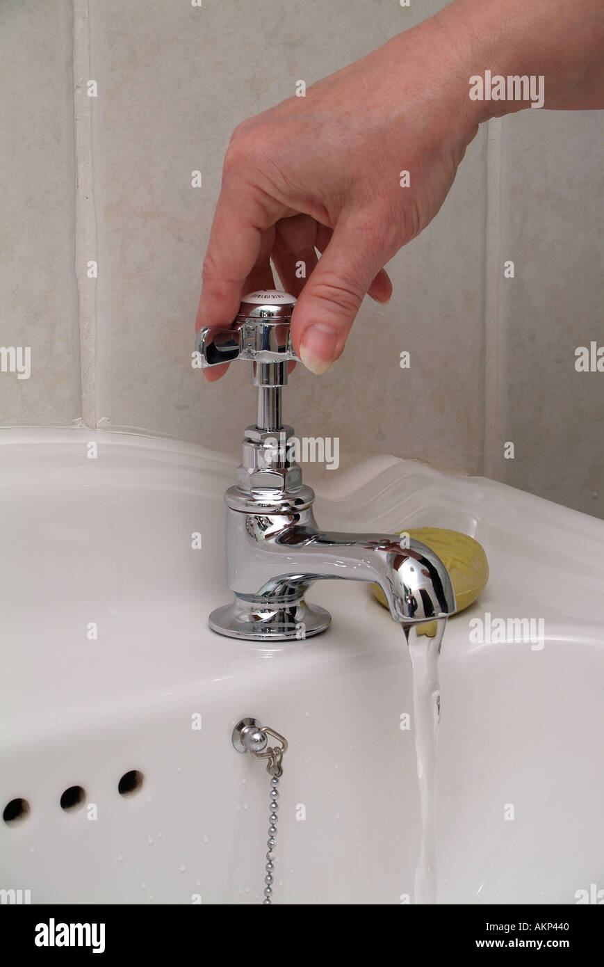 La main de femme au détour d'une salle de bains chrome robinet sur évier bassin Banque D'Images