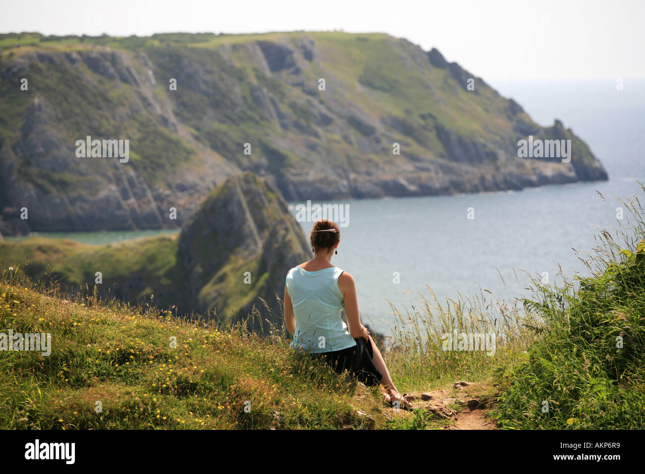 Hommes célibataires femme jeune femme assise sur une falaise pittoresque chemin des falaises surplombant la baie de trois Gower Wales UK Banque D'Images