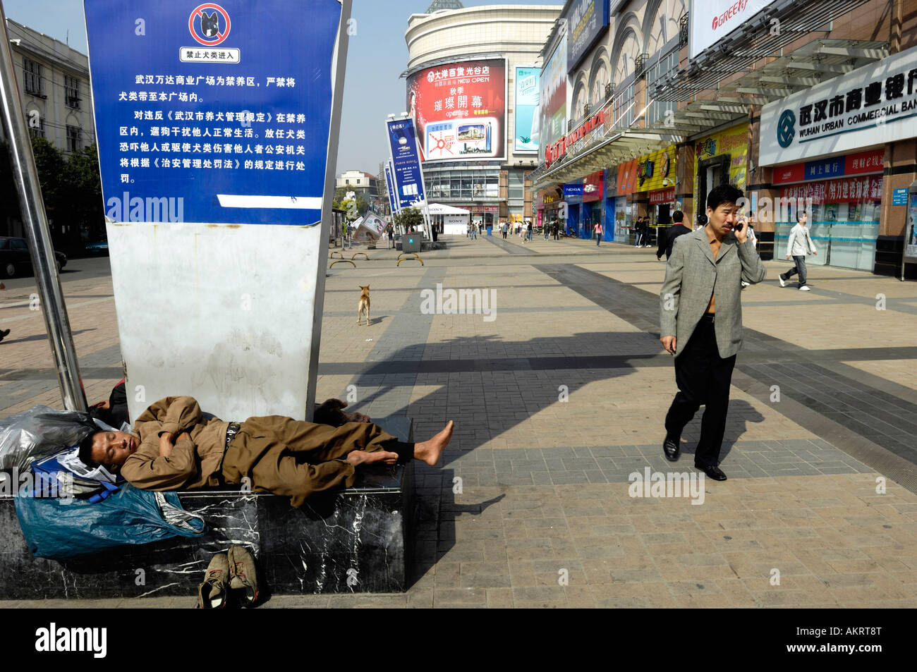 Un vagabond de dormir alors qu'un homme parlant avec téléphone cellulaire dans une rue commerciale de Wuhan Hubei Chine 21 Oct 2007 Banque D'Images