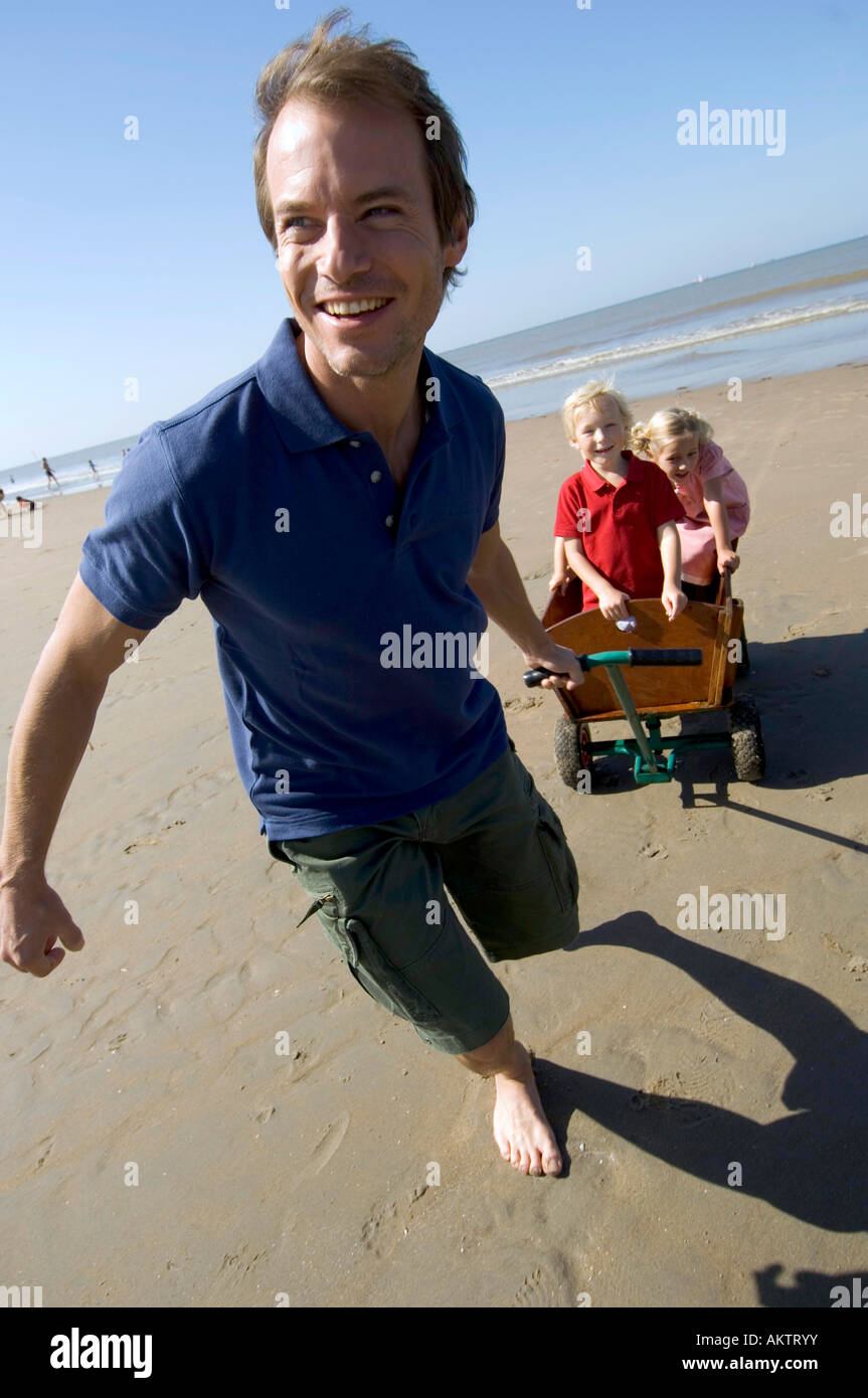 Père tirant charrette avec les enfants sur la plage Banque D'Images