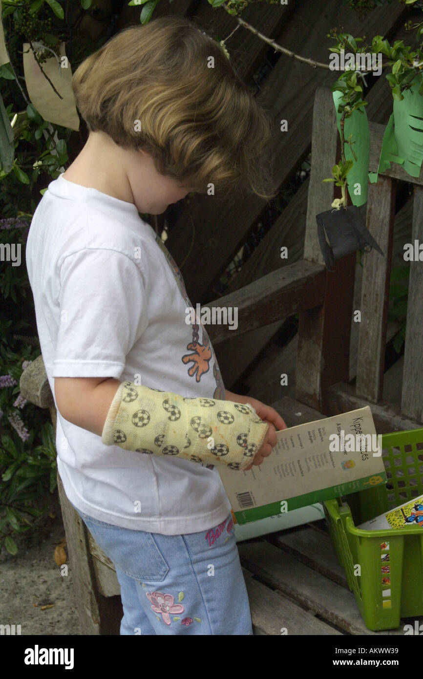 Jeune fille lisant avec un bras dans un plâtre Banque D'Images