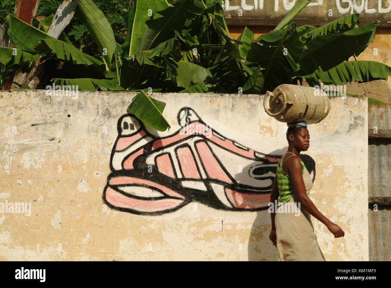 Une femme portant une bouteille de gaz sur sa tête passe devant un mur avec  un graffiti d'un Adidas trainer. L'Inhambane, au Mozambique Photo Stock -  Alamy