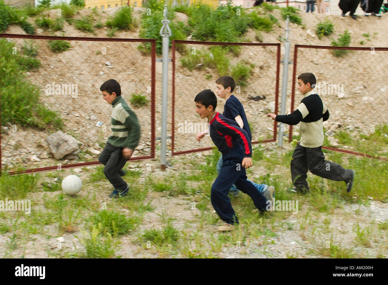 L'ARMÉNIE Vanadzor quatre garçons d'âge scolaire jouer au soccer à l'extérieur dans une aire de jeux clôturée de mauvaises herbes s'exécuter après ball dans le groupe Banque D'Images