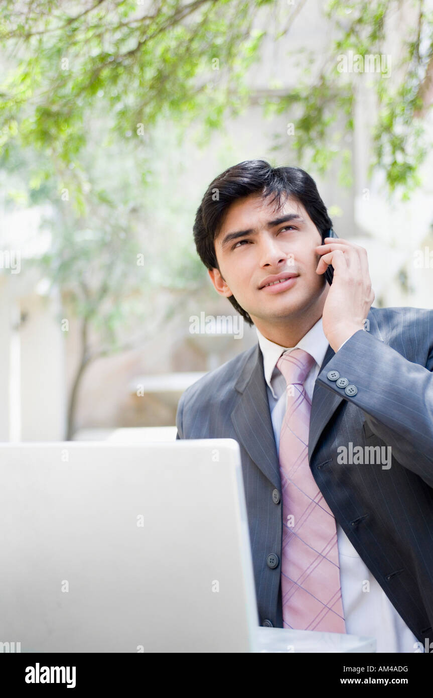 Businessman standing in front of a laptop and talking on a mobile phone Banque D'Images