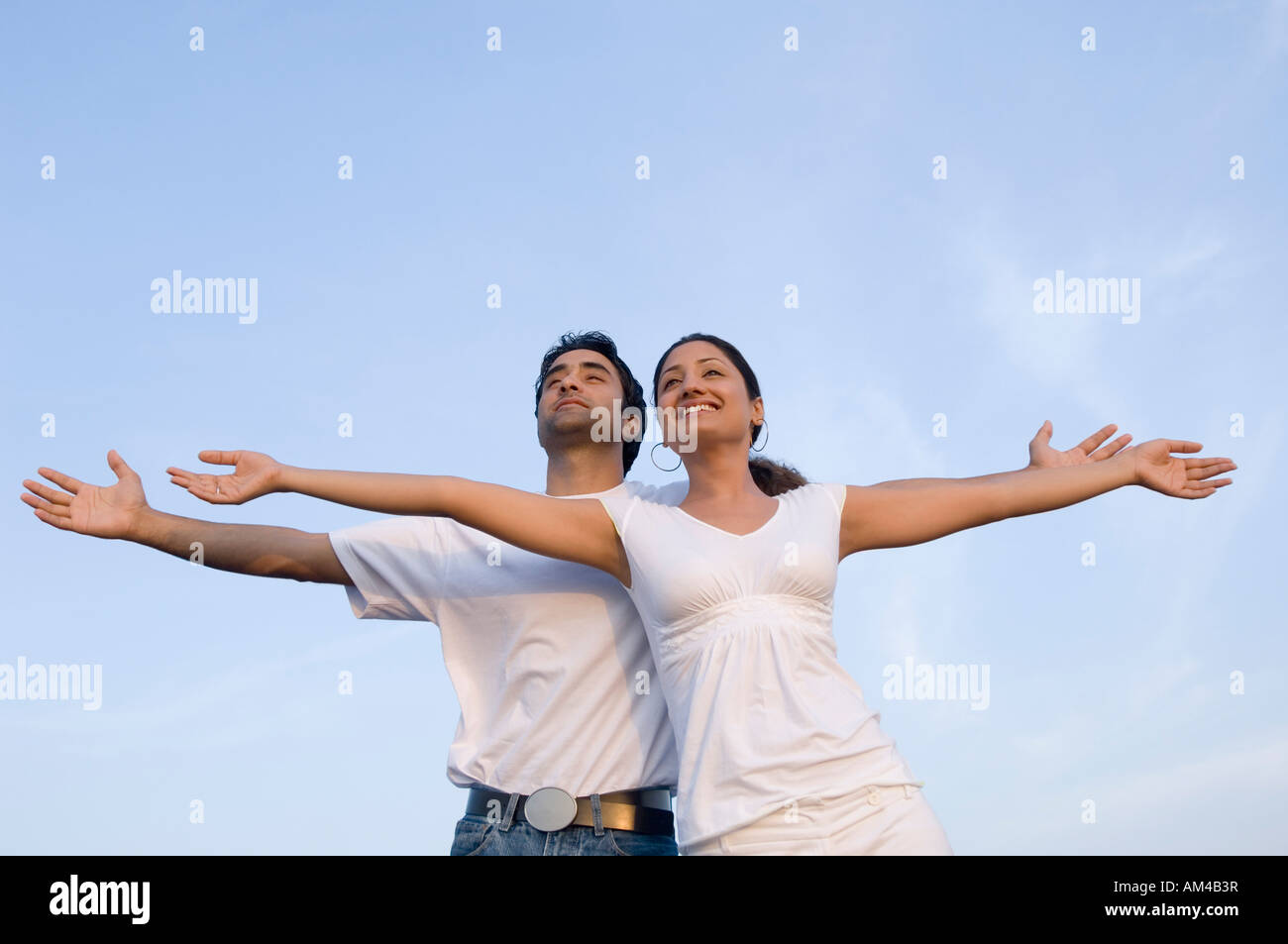 Low angle view of a young couple avec leurs bras tendus et souriant Banque D'Images