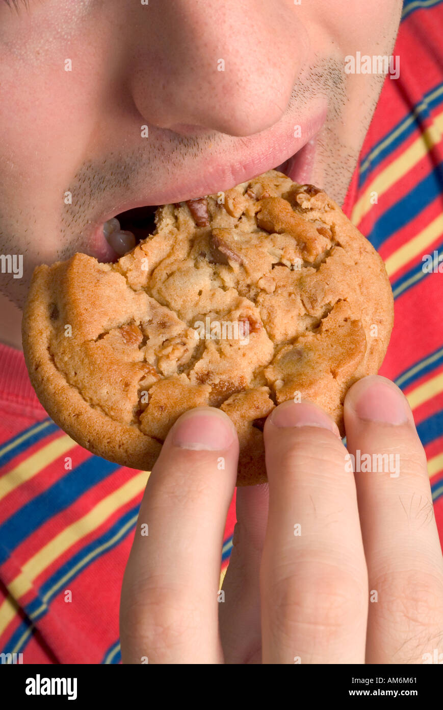 Jeune homme en chemise de couleur vive de manger un gros cookie Banque D'Images