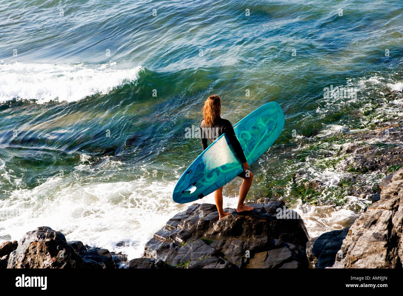Femme debout avec un surf sur de grosses roches. Banque D'Images