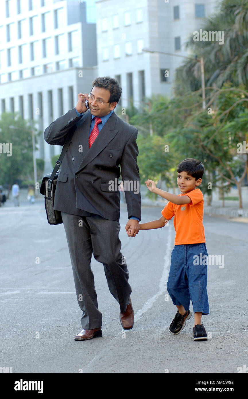 Père et fils jeune Indien executive en costume avec un sac d'ordinateur portable talking on mobile phone marche sur route en Inde Mumbai BKC DE LA CDB Banque D'Images