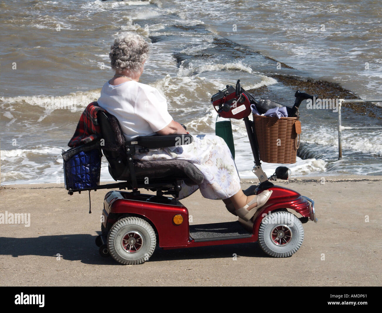Front de mer promenade de mur de mer femme mature conduisant sur scooter d'invalidité motorisée regardant à marée haute mer rugueuse Walton sur le Naze Essex Angleterre Royaume-Uni Banque D'Images