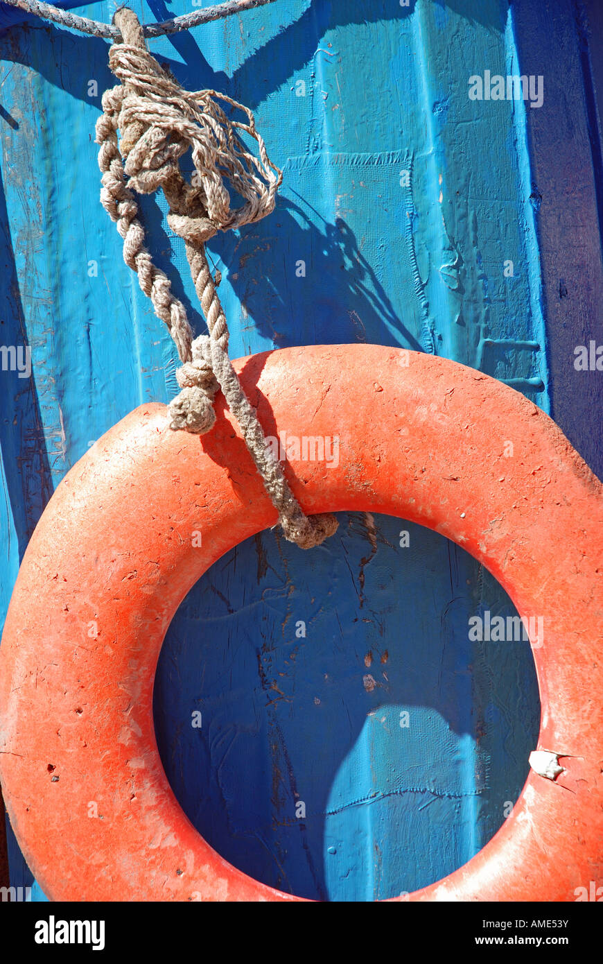 Bouée Orange se balançant sur une corde effilochée attaché à la barre d'un bateau bleu en plein soleil. Banque D'Images