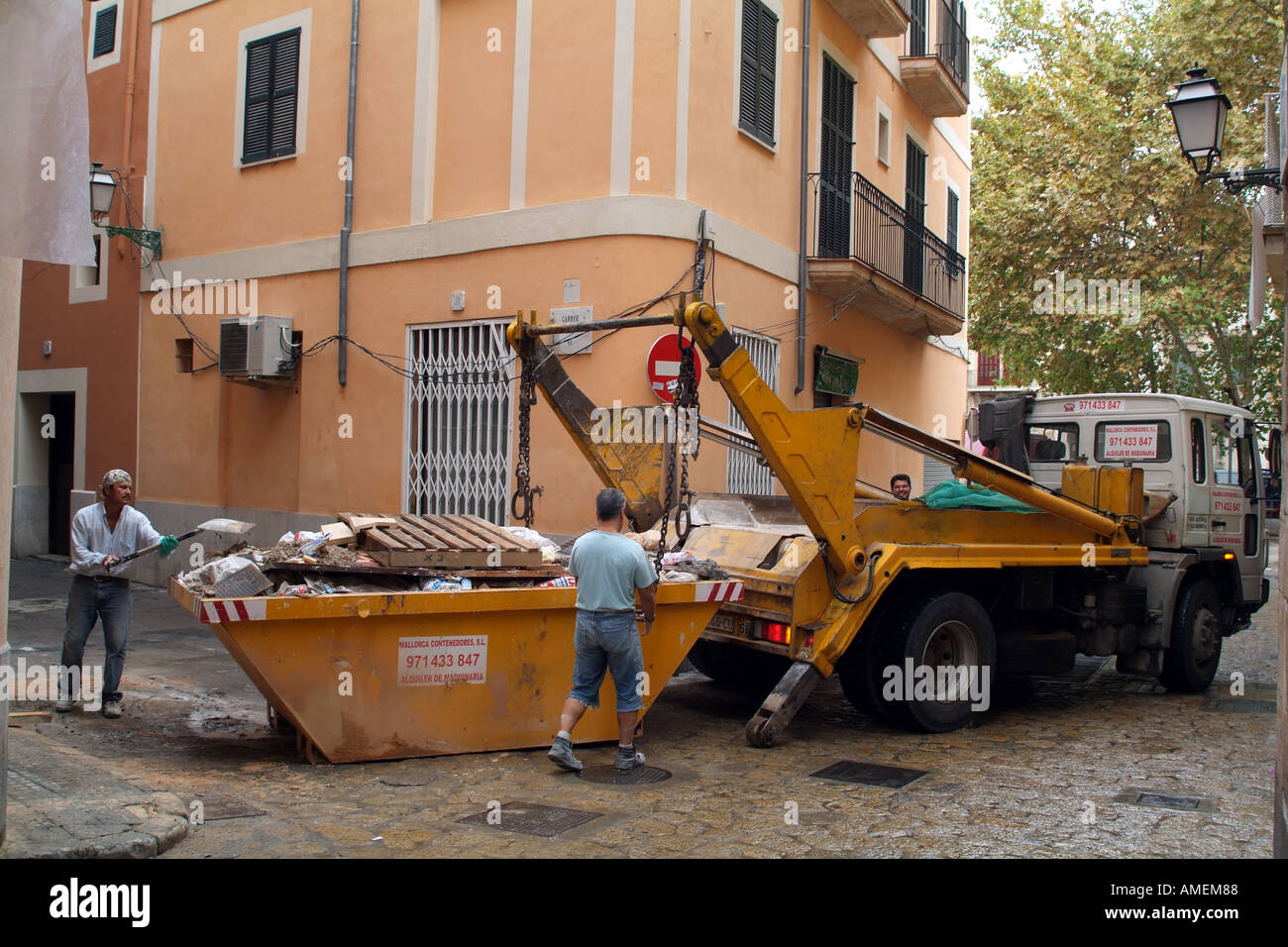 Builders skip loading gravats ordures camion sur la rue étroite Banque D'Images