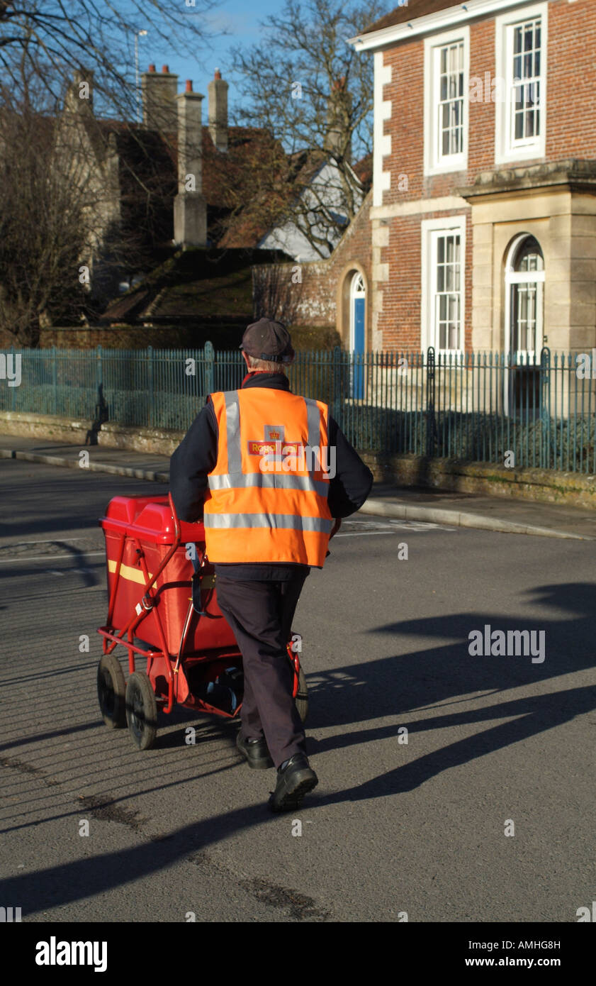 Facteur poussant son chariot rouge contenant du courrier sur son cycle de livraison à Salisbury Wiltshire England UK Banque D'Images