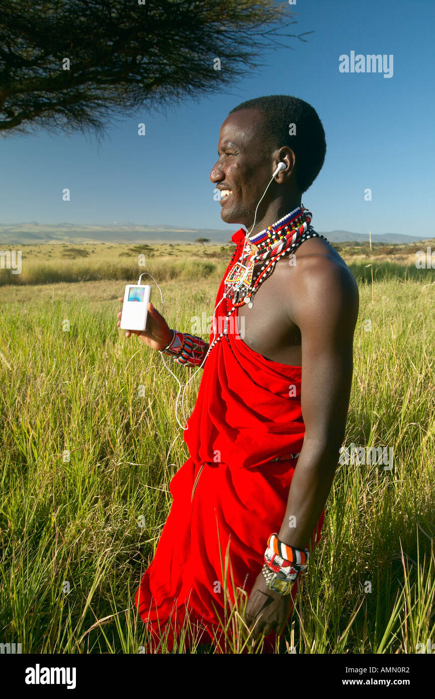 Guerrier masaï près de l'arbre d'Acacia d'écouter de la musique sur l'iPod par Apple en rouge paysage d'arpentage de Lewa Conservancy Kenya Afrique Banque D'Images