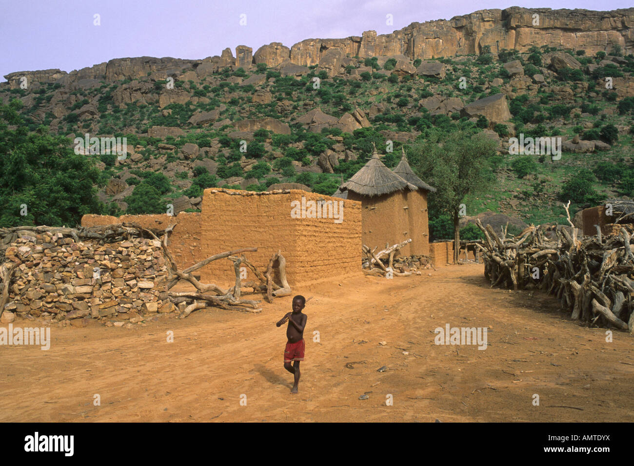Petit garçon marchant le long d'une route poussiéreuse dans un village Dogon avec l'escarpement de Bandiagra dans l'arrière-plan Banque D'Images