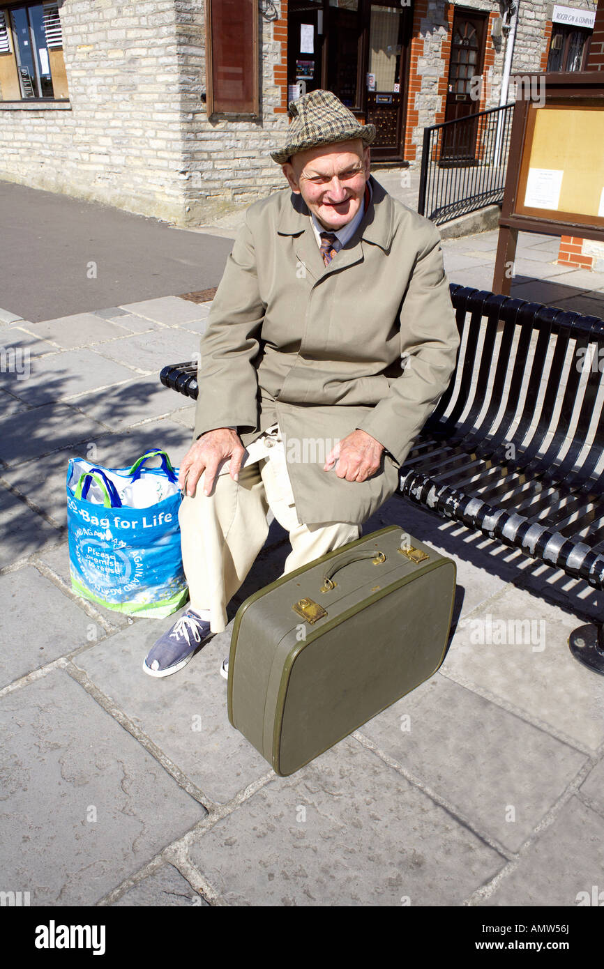 Vieil Homme avec chapeau imperméable et valise assis sur un banc, pauvres voyageurs de banlieue Somerton propre Angleterre Somerset Banque D'Images