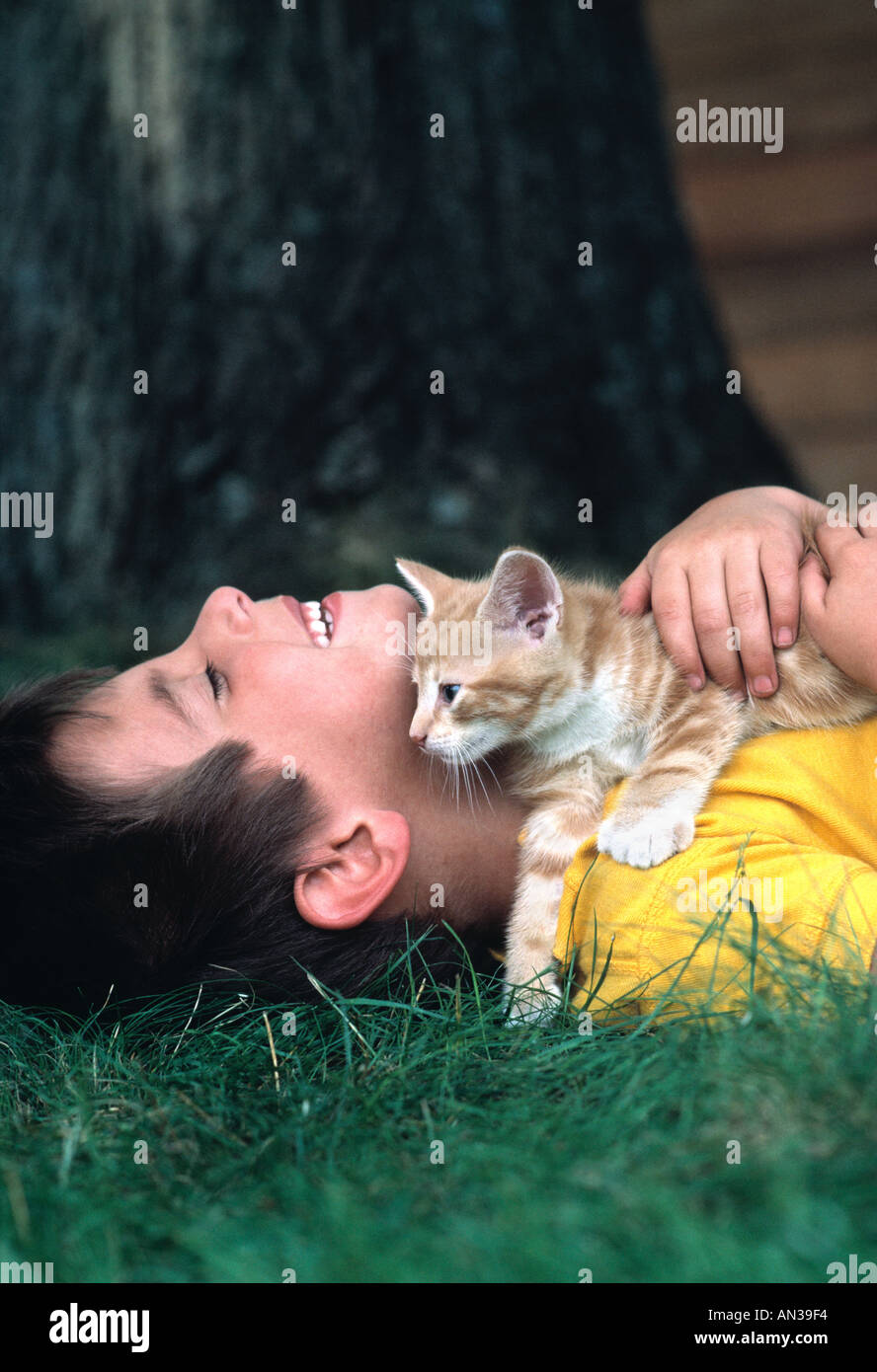 Un garçon de six ans qui s'est posé dans l'herbe tenant son chat animal de compagnie Banque D'Images